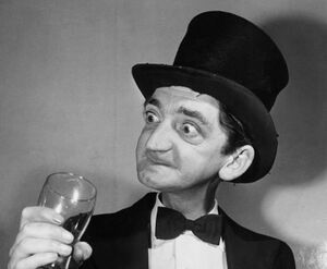 A black and white photo of a thin gentleman in a top hat and dickie-bow, holding a pint glass